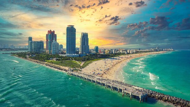 A coastal cityscape with a pier extending into turquoise waters, surrounded by high-rise buildings and a beach. - 5BR HotTub / PoolTable / MiniGolf / 7  min to Wynwood (Miami)