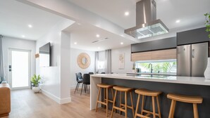 A modern kitchen with a central island, bar stools, and a stainless steel refrigerator. - 5BR HotTub / PoolTable / MiniGolf / 7  min to Wynwood (Miami)