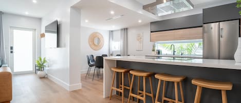A modern kitchen with a central island, bar stools, and a stainless steel refrigerator.