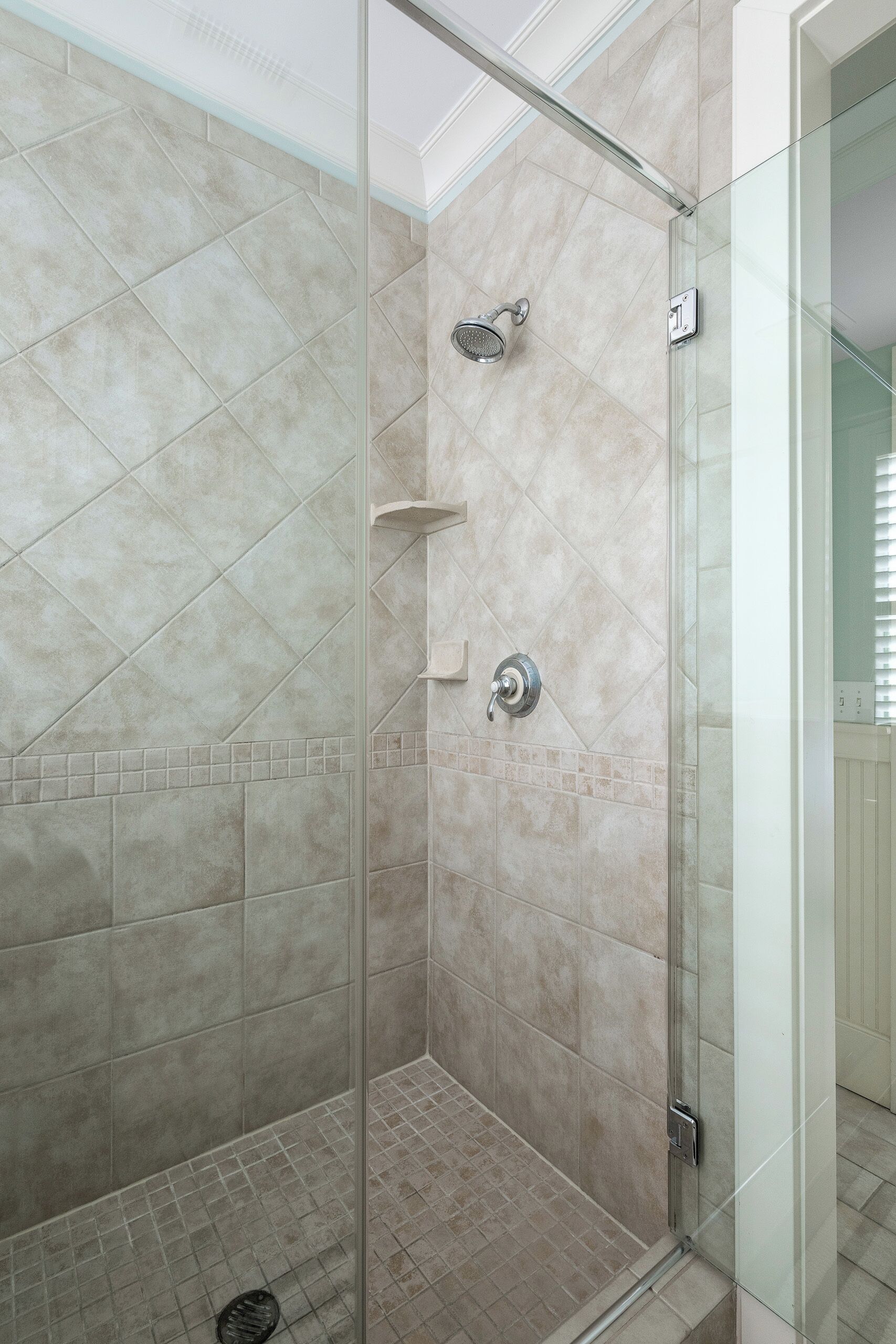 A glass-enclosed shower with beige tiles and a visible showerhead.
