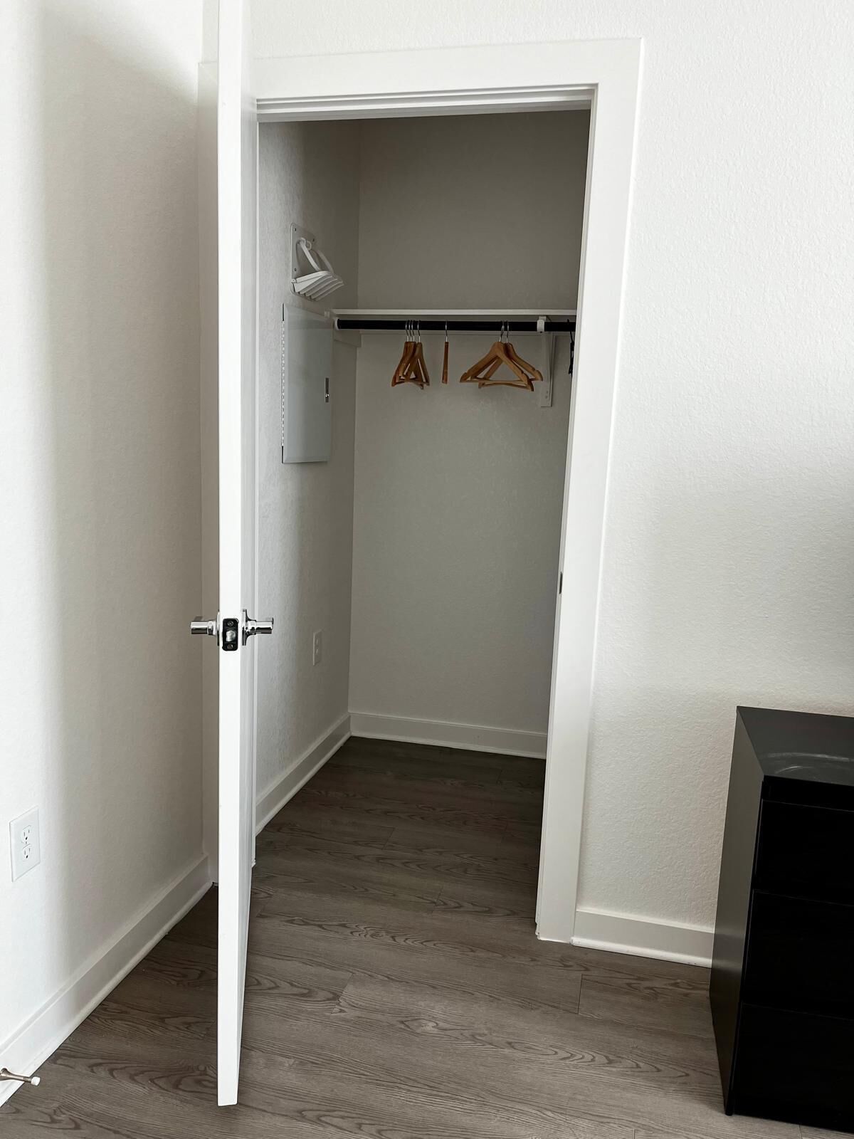 Un dressing accessible sans porte, doté d’un plancher en bois, d’une porte blanche et d’un porte-manteau avec des cintres.