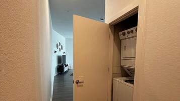 Un pasillo estrecho con suelo de madera que conduce a un área de lavandería con lavadora y secadora.