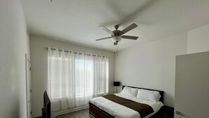 Ein Schlafzimmer mit einem Bett, einem Deckenventilator und einem Fenster mit Jalousien.