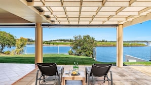 An outdoor patio with two chairs and a table, overlooking a body of water and a distant landscape.