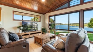 A spacious living room with a large flat-screen TV, leather sofas, wooden coffee table, and a telescope.