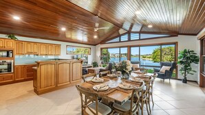 A spacious kitchen with wooden cabinets, a dining area with a table set for four, and a view of a lake through large windows.