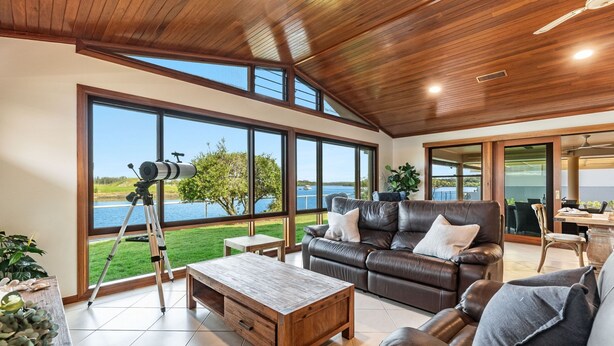 A spacious living room with a large window overlooking a lake, a telescope, and a leather sofa.