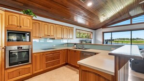 A modern kitchen with wooden cabinets, stainless steel appliances, and a large window offering a view of the outdoors.