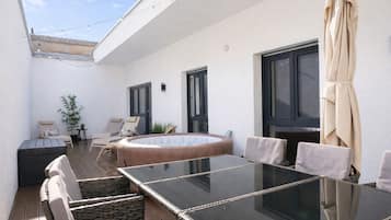 An outdoor patio with a glass table, wicker chairs, a hot tub, and a potted plant.