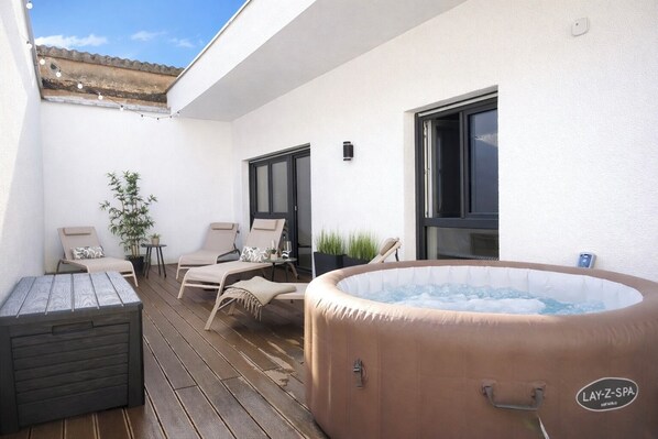 An outdoor patio with a hot tub, lounge chairs, and a small table.