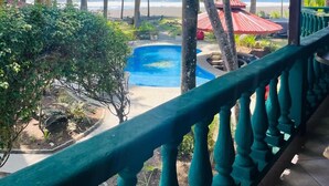 Ein Poolbereich mit Blick auf Strand und Meer, umgeben von Palmen und einem überdachten Gang.