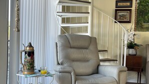 Un saló amb un sofà de pell gris, una taula petita amb una gerra decorativa i una escala amb barana blanca.