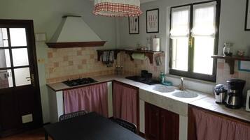 Une cuisine de taille réduite, équipée d’une cuisinière à gaz, de deux éviers, d’une table à manger et d’une fenêtre avec des rideaux.
