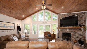 A spacious living room with a high ceiling, a fireplace, a large TV, and a cozy seating area.
