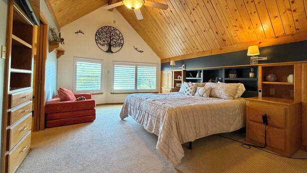 A bedroom with a sloped ceiling, a ceiling fan, a bed with white bedding, a red chair, and a dresser with a lamp. - Yosemite Chalet, Golf Course Views, Game Room, Walk to Lake, Sleeps 12 (Groveland)