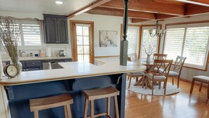 A kitchen with a central island, wooden stools, and a dining area with chairs. - Yosemite Chalet, Golf Course Views, Game Room, Walk to Lake, Sleeps 12 (Groveland)