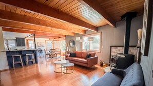 A spacious living area with a wooden ceiling, a fireplace, a sofa, a coffee table, and a dining area with chairs and a table. - Yosemite Chalet, Golf Course Views, Game Room, Walk to Lake, Sleeps 12 (Groveland)