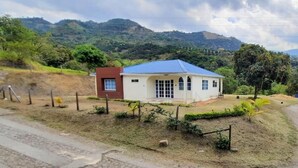 Une petite maison avec un toit bleu et une partie rouge, entourée d’une clôture et de verdure.