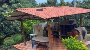 Une terrasse extérieure avec un toit recouvert de tuiles rouges, une table ronde et un barbecue.