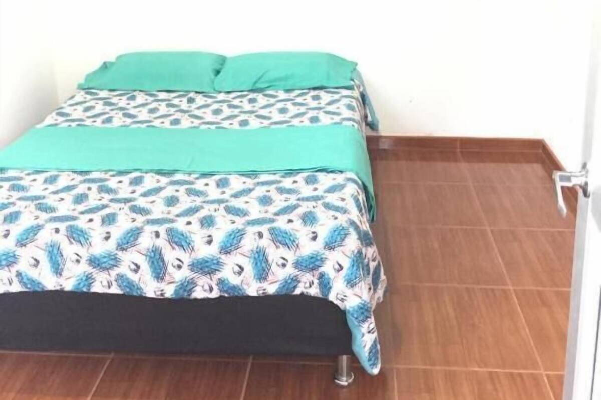 Una habitación pequeña con cama individual, colcha estampada, almohadas turquesa y suelo de madera.