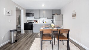 A modern kitchen with grey cabinets, stainless steel appliances, and a dining area with a wooden table and chairs. - Cozy den in Columbus (Columbus)
