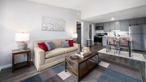 A modern living room with a sofa, coffee table, and a dining area with chairs and a kitchen in the background. - Cozy den in Columbus (Columbus)
