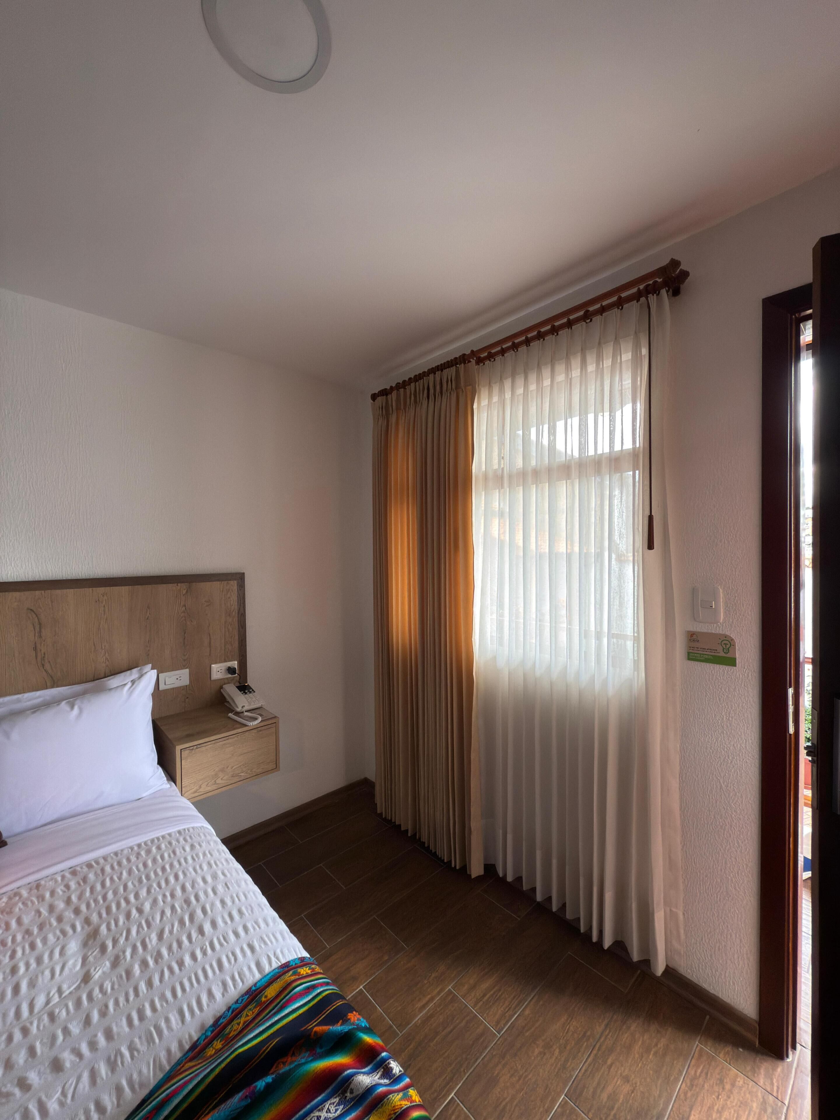 Une chambre d’hôtel avec un lit, une table de chevet et une fenêtre avec des rideaux.