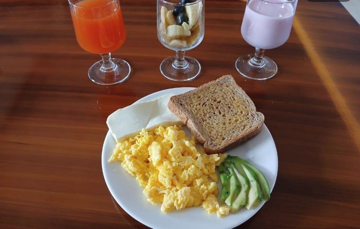 A breakfast plate with scrambled eggs, avocado, and toast, accompanied by three drinks on a wooden table.