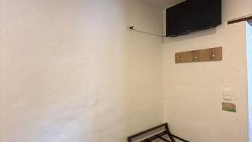 Una habitación con paredes blancas, suelo de madera, televisor montado, tendedero y un estante de madera con ganchos.