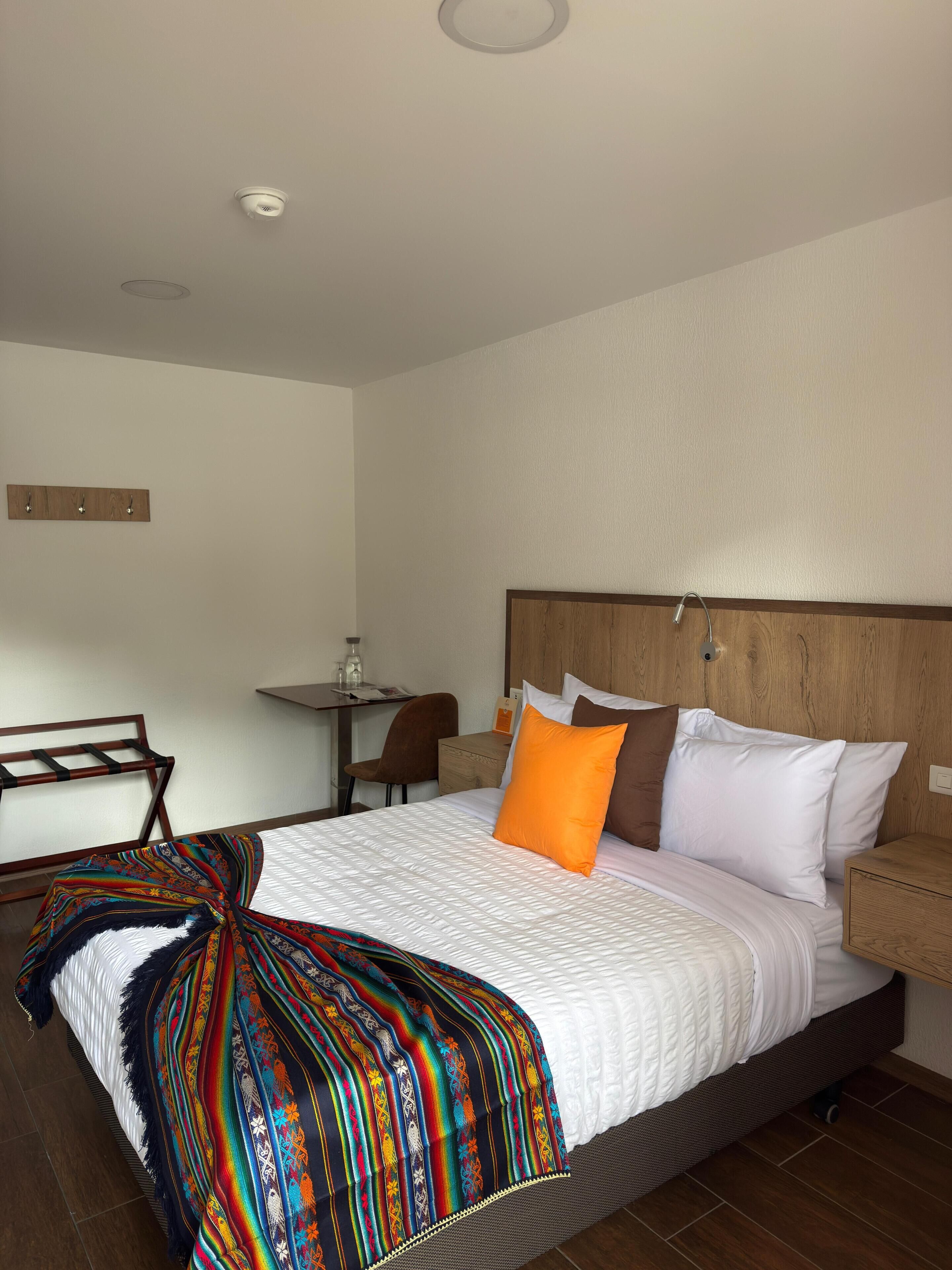 A hotel room with a bed, a desk, a chair, and a small table.