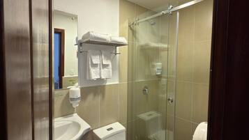 Un baño moderno con ducha envuelta en vidrio, inodoro blanco, lavabo y espejo.