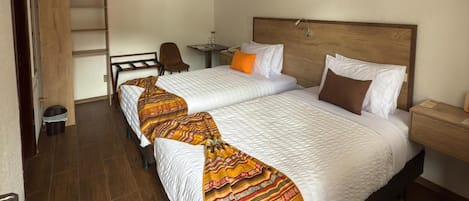 Habitación de hotel con dos camas, un escritorio, una silla y una mesita.