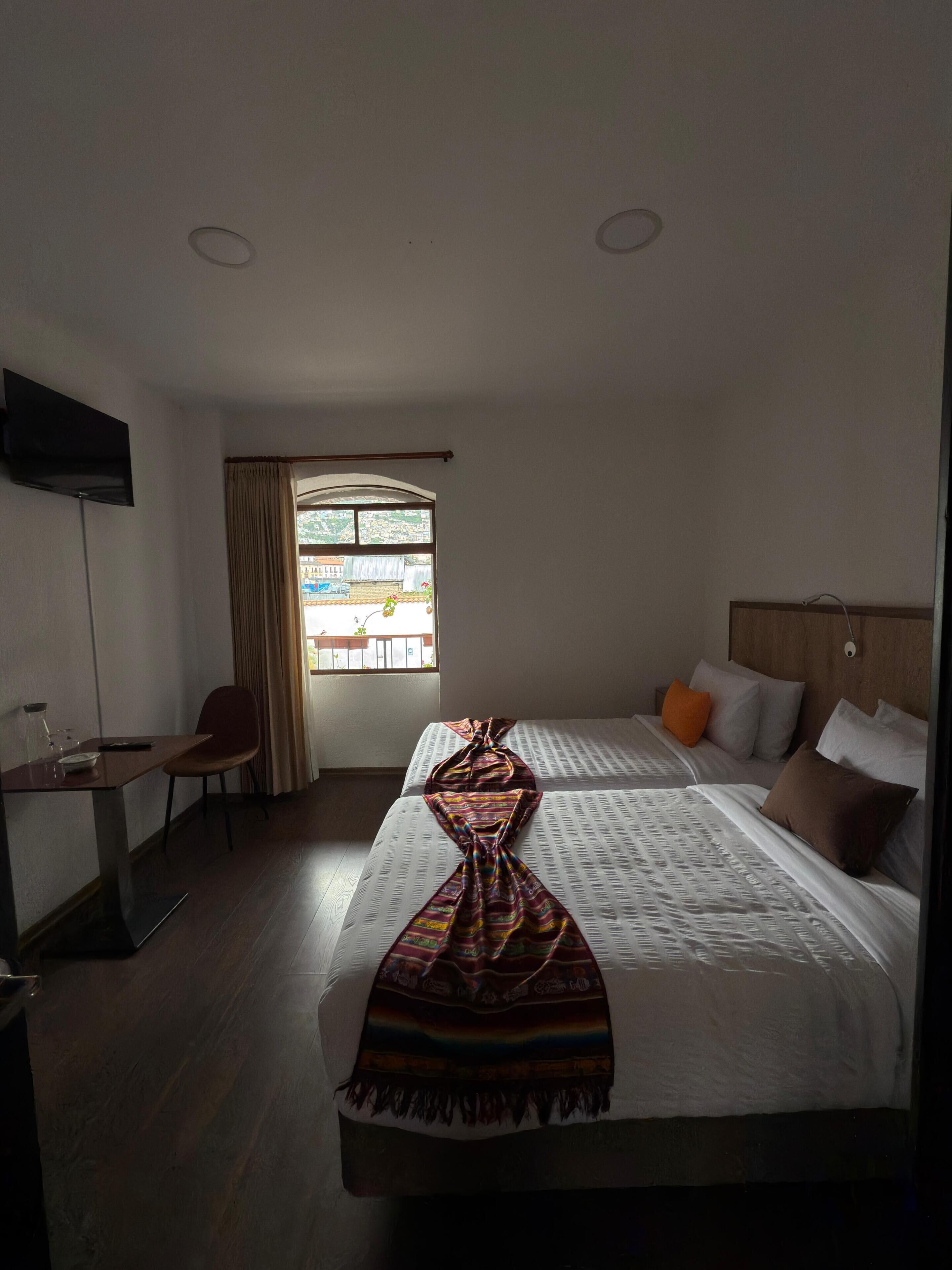 A hotel room with two beds, a desk, a chair, a TV, and a window with curtains.