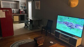 Un salon avec une table basse en bois, un téléviseur, un réfrigérateur rouge et une cuisine à l’arrière-plan.