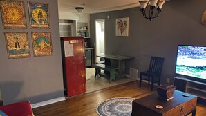 Un salon avec un plancher en bois, un réfrigérateur rouge, une télévision et un canapé aux couleurs vives.