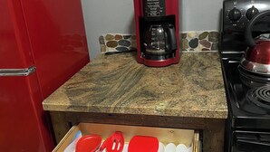 Une cuisine avec un réfrigérateur rouge, une machine à café et un tiroir contenant des ustensiles de cuisine.