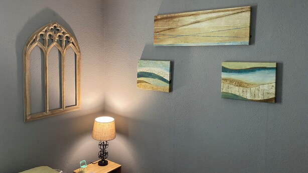 Une pièce comprenant une table de chevet en bois, une lampe et trois tableaux accrochés au mur.