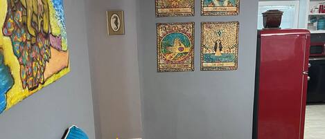 Una sala de estar con un sofá de colores, un refrigerador rojo y una pared con cuatro obras de arte enmarcadas.