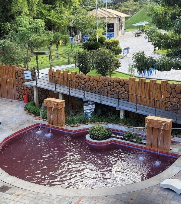 Une piscine bordée d’un mur en pierre et dotée d’une terrasse en bois, entourée de verdure et agrémentée d’un espace salon abrité.