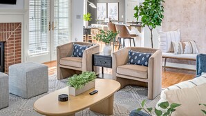 Un salon moderne avec une cheminée, deux fauteuils, une table basse et, au fond, un coin repas.