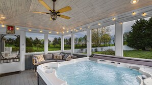 Un espace extérieur abrité avec un jacuzzi, un ventilateur de plafond, un canapé avec des coussins et une vue sur un terrain de golf.