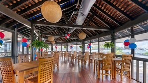Un vaste espace dédié à la salle à manger, avec des tables et des chaises en bois, de grandes fenêtres et une vue sur l’eau.
