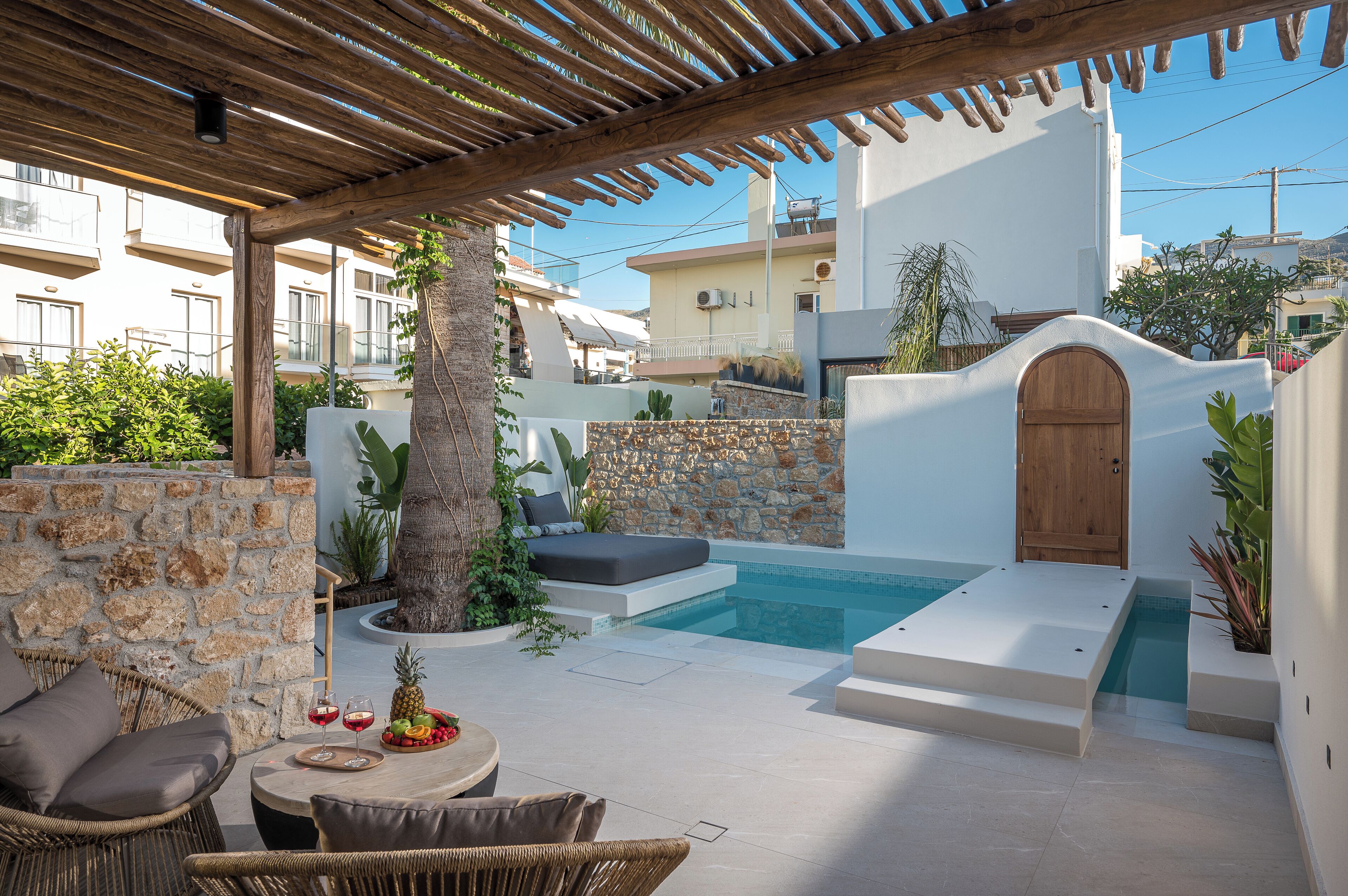 Ein moderner Poolbereich im Freien mit einer Holzpergola, Steinmauern und einer Sitzecke mit Kissen.