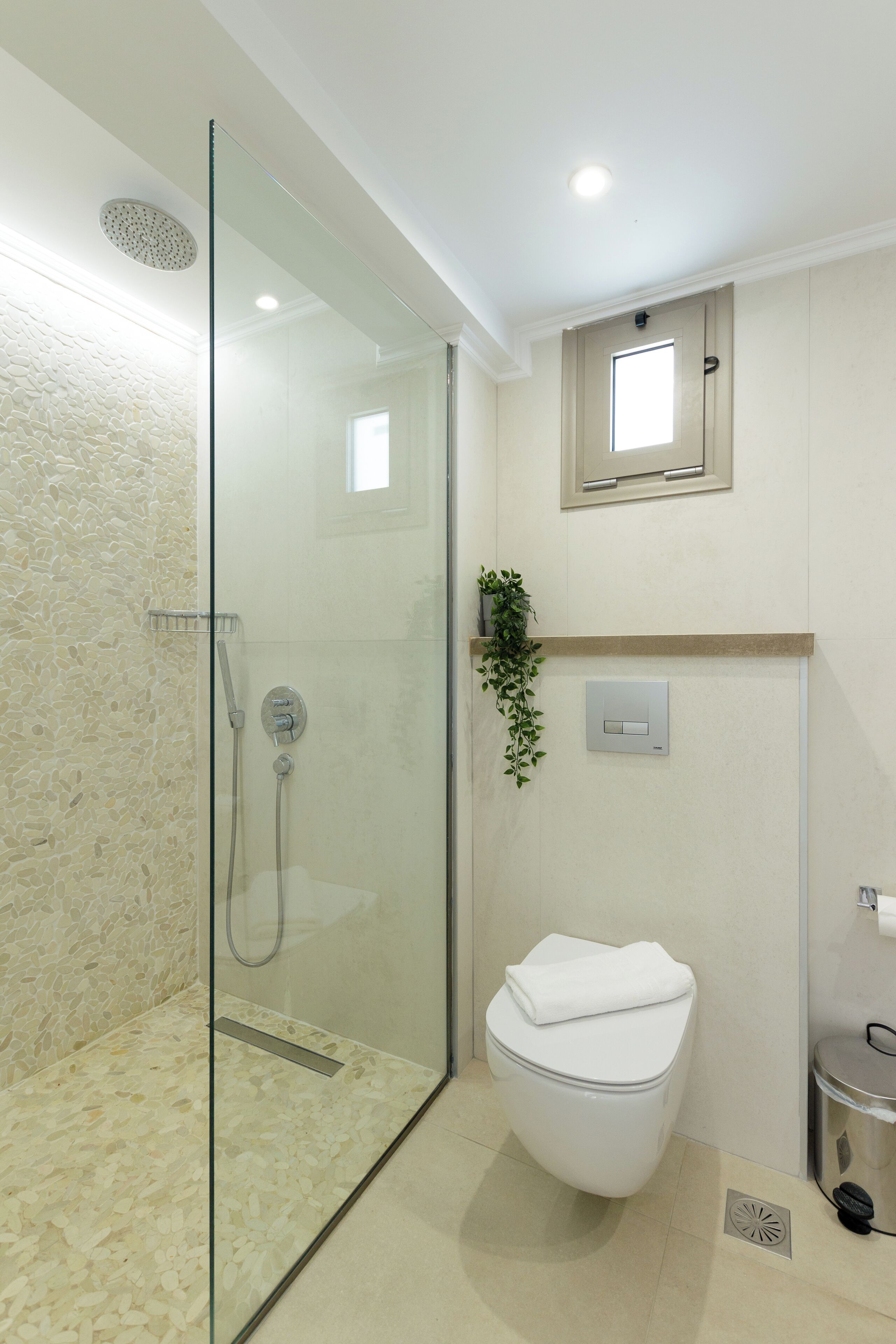 A modern bathroom with a glass-enclosed shower, a white toilet, and a small trash bin.