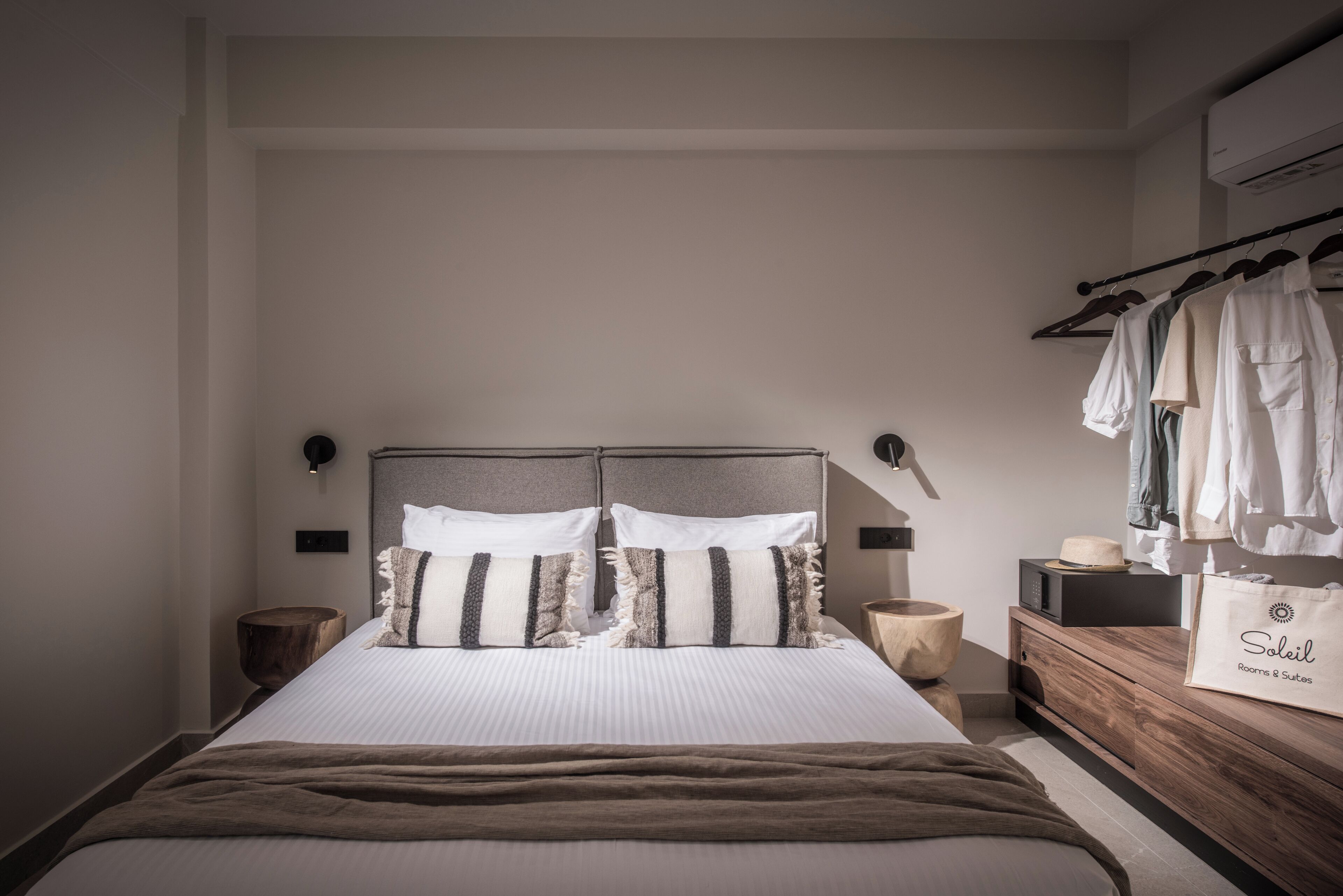 A neatly arranged bedroom with a large bed, bedside tables, a wooden dresser, and a clothing rack.