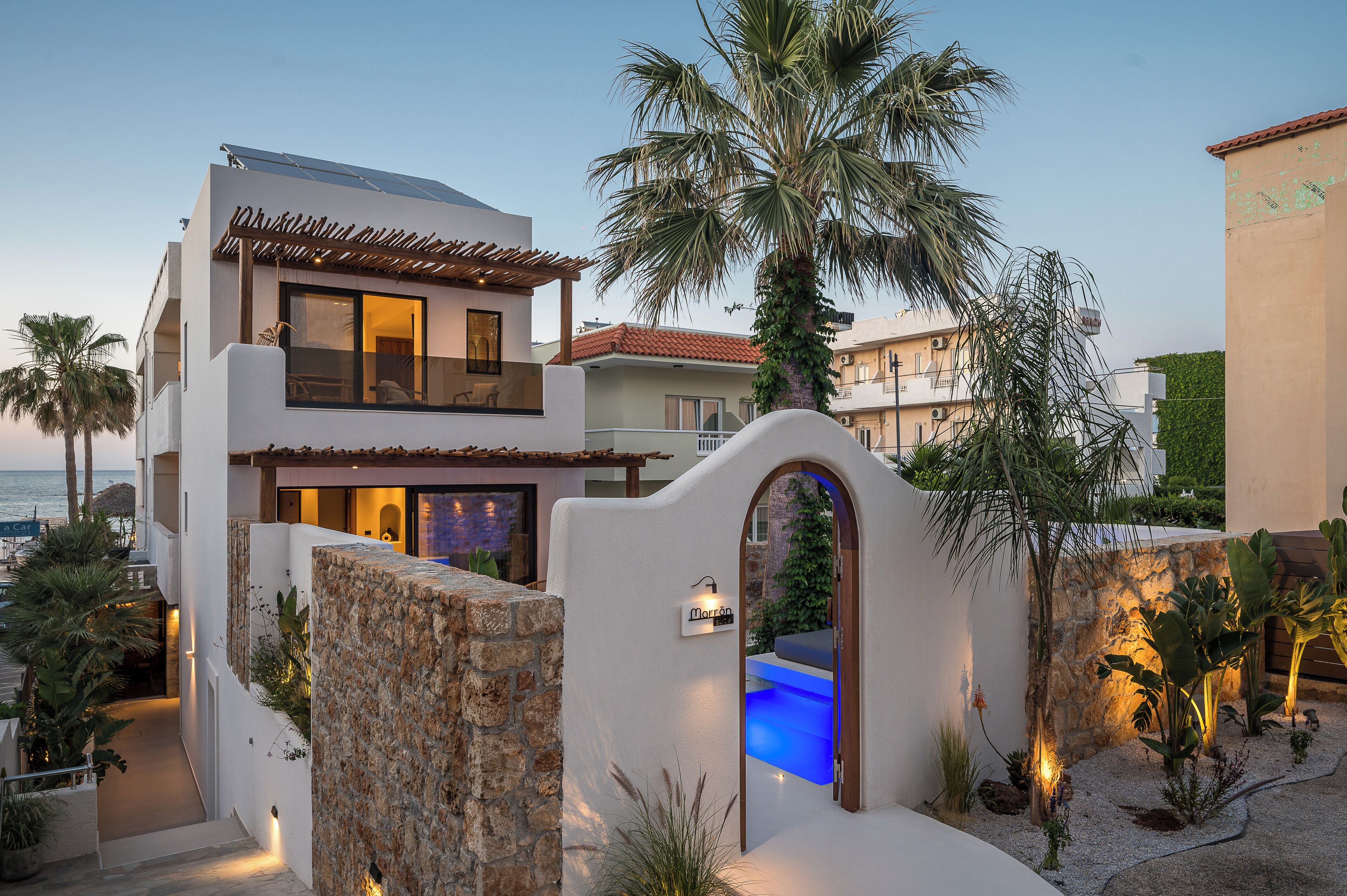 Una casa moderna de dos pisos con muro de piedra, piscina y vista al mar.