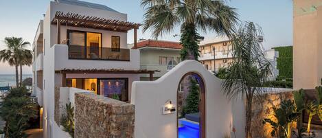 Una casa moderna de dos pisos con muro de piedra, piscina y vista al mar.