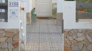 A small, white building with a tiled roof, a stone wall, and a metal gate. - Villa Sonho do Mar - Villa with Saltwater Pool (Vale da Telha)
