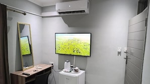 Un baño moderno con un espejo grande, un televisor de pantalla plana, una cafetera y un equipo de aire acondicionado.