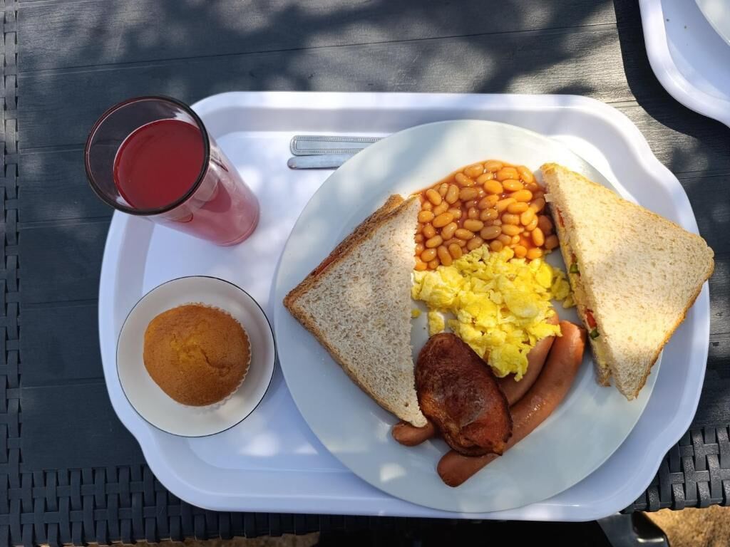 A tray with toast, beans, sausages, scrambled eggs, and a glass of red drink.